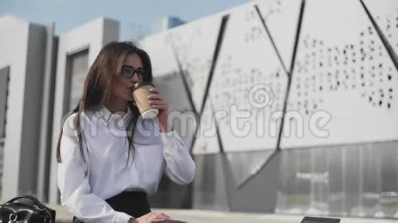 漂亮的商务女性戴着眼镜在智能手机上说话喝着咖啡现代背景建设视频的预览图