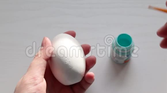 女用手画一个白色的鸡蛋上面涂着蓝色的颜料以备节日之用复活节的概念视频的预览图