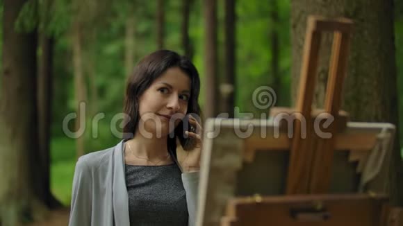 女孩艺术家在森林里画一幅画用手机聊天视频的预览图