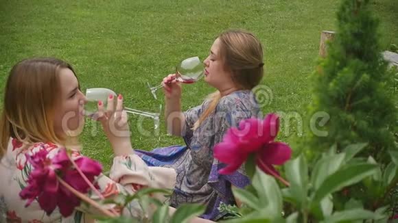 美丽优雅的女人喝着红酒享受着在美丽的夏日花园里盛开牡丹的假期视频的预览图