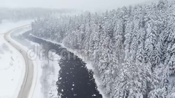 冬季在河流附近的乡村公路和降雪期间的针叶林的空中景色冬季的概念视频的预览图