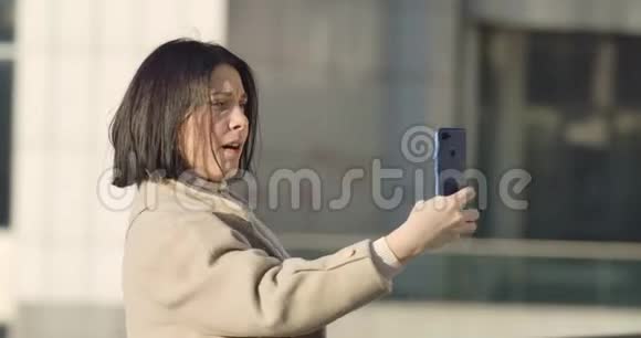 侧视深色白种人妇女做脸和自拍照片积极的年轻女士使用智能手机视频的预览图