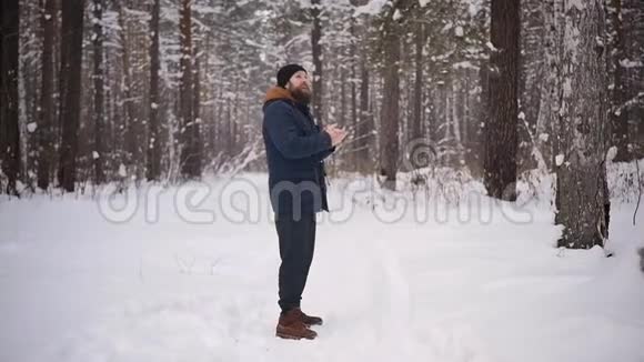 一个留着胡子的人在冬天的森林里在他的嘴附近温暖了他的双手寒冷的天气冻僵的手冬季天气视频的预览图