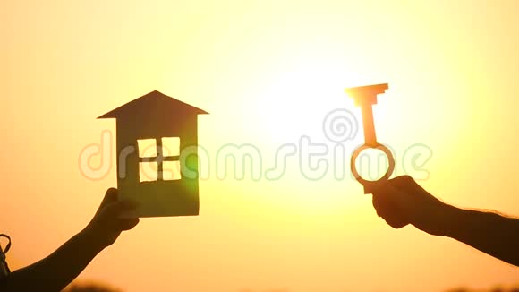 纸屋和钥匙的剪影一个人拿着钥匙对着日落一个女人手里拿着房子视频的预览图