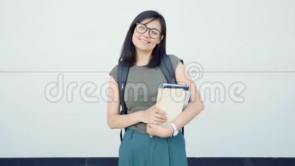 年轻女子带着书和背包拇指在灰色背景上视频的预览图