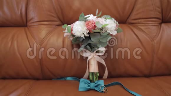 漂亮的结婚花束躺在沙发上戴着结婚戒指和新郎的领结视频的预览图
