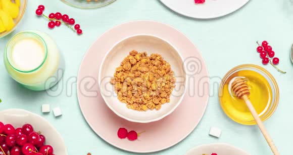 在蓝色背景的粉红色陶瓷碗中加入巧克力覆盆子芒果辣椒籽和牛奶的格兰诺拉麦片视频的预览图