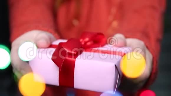 女性手拿着带有红色丝带的惊喜礼盒前景模糊的花环新年快乐生日快乐视频的预览图