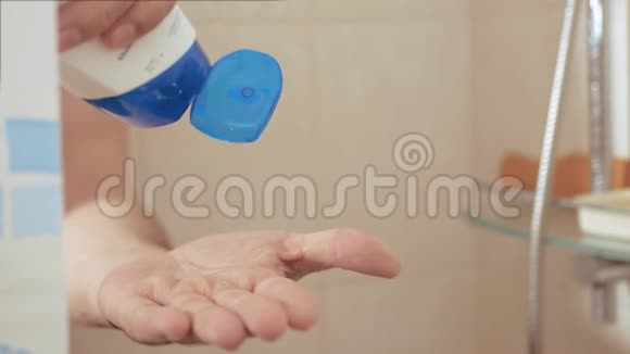男性手从白色瓶蓝色瓶盖上挤压淋浴凝胶慢动作并关闭视频的预览图
