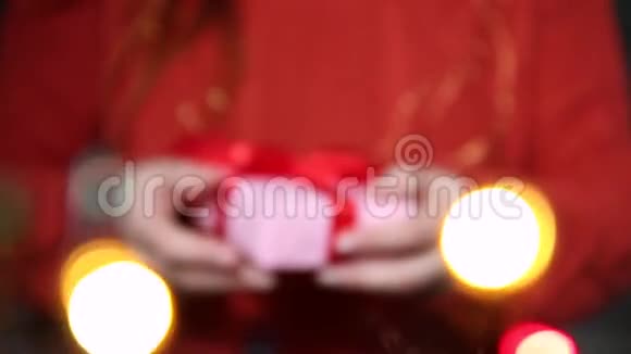 女性手拿着带有红色丝带的惊喜礼盒前景中模糊的花环视频的预览图