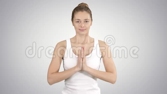 年轻的瑜伽女性练习瑜伽做纳马斯特手势锻炼身体穿白色t恤在梯度背景上视频的预览图