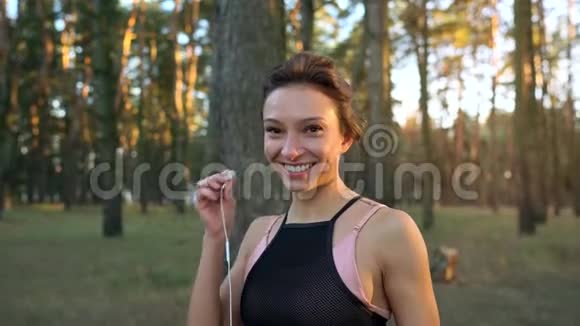 微笑的女人把耳机插入耳朵在日落时穿过秋天的森林慢动作视频的预览图