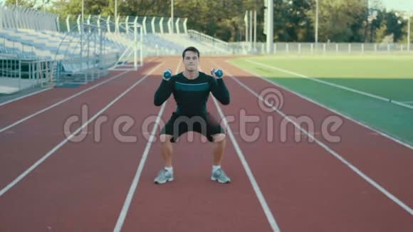 年轻的肌肉男运动员在体育场里用哑铃做蹲视频的预览图