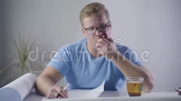 年轻的白种人建筑师坐在桌子旁咬着苹果记着蓝图专业设计师视频的预览图