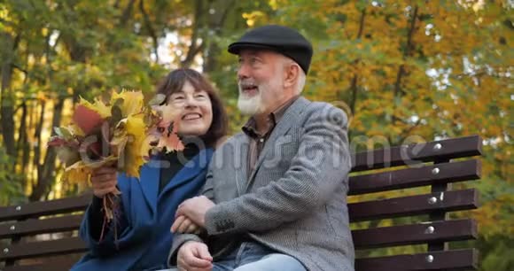 快乐的老年夫妇喜欢坐在长凳上的户外活动妻子捧着一束秋叶丈夫视频的预览图