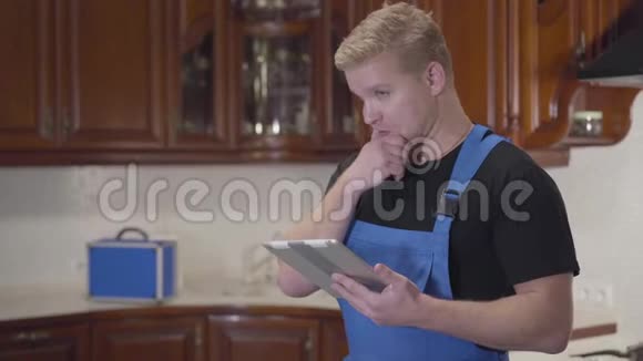 年轻的白种人杂工站在厨房拿着平板电脑环顾四周的肖像红头发的人想修理视频的预览图