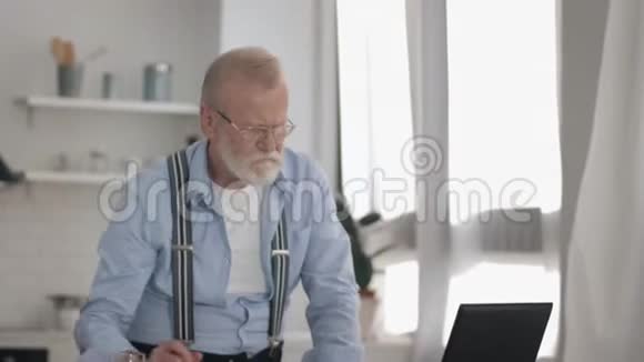 有视力眼镜的现代老年男性养老金领取者在手提电脑饮料果汁上辛勤工作视频的预览图