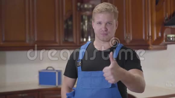穿着工袍的年轻白种人杂工站在厨房竖起大拇指的肖像英俊自信的男人视频的预览图