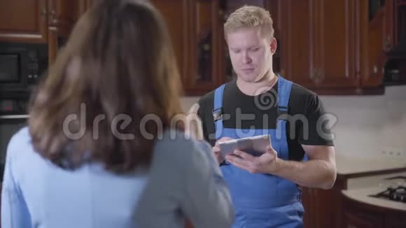 年轻英俊的白种人男子的肖像穿着蓝色长袍拿着平板电脑听着黑发女人无法辨认视频的预览图