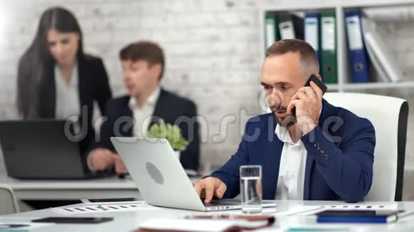 忙碌的男性上班族在现代工作场所使用智能手机输入笔记本电脑文本视频的预览图