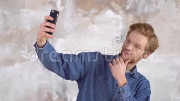 年轻的红发男子被隔离在彩绘的墙上拍着欢快的自拍照片视频的预览图