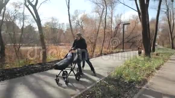 秋天一个年轻的家庭在阳光明媚的城市公园里带着婴儿车在溜冰鞋上散步爸爸开另一辆车视频的预览图