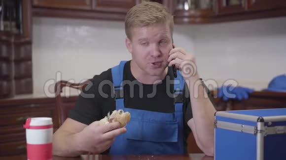 年轻白种人水管工在智能手机和吃三明治上与顾客交谈的肖像红头发的家伙视频的预览图