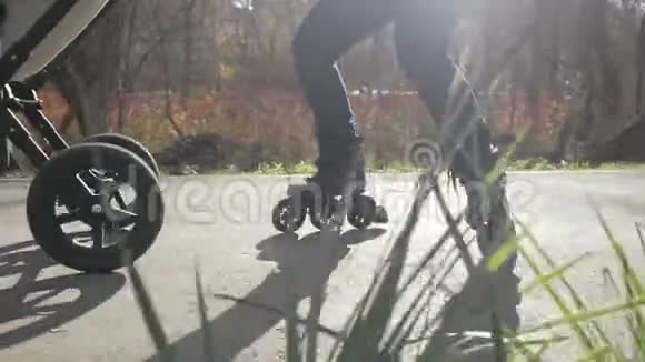 年轻的家庭轮滑与他们的孩子在婴儿车在美丽的秋天公园爸爸骑着后轮向后走视频的预览图