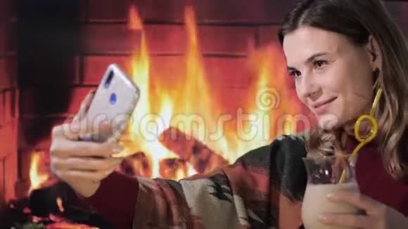 年轻的微笑女性在智能手机上自拍壁炉背景上手里拿着传统的鸡蛋鸡尾酒视频的预览图