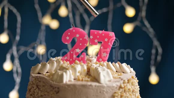 生日蛋糕有27个数字由较轻的粉红色蜡烛燃烧在蓝色的背景上蜡烛被点燃了慢动作视频的预览图