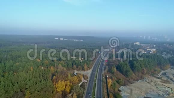 空中无人机镜头飞越高速公路附近的森林与城镇的地平线视频的预览图
