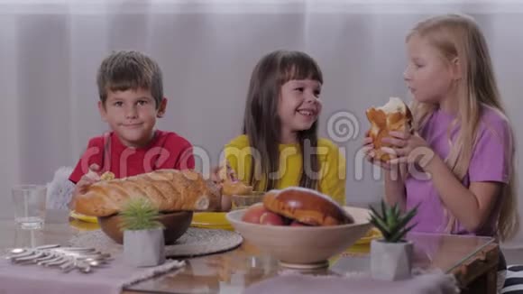 无忧无虑的童年快乐的男孩和微笑的女孩坐在甜蜜的桌子上在节日的孩子们聚会后吃芳香的糕点视频的预览图