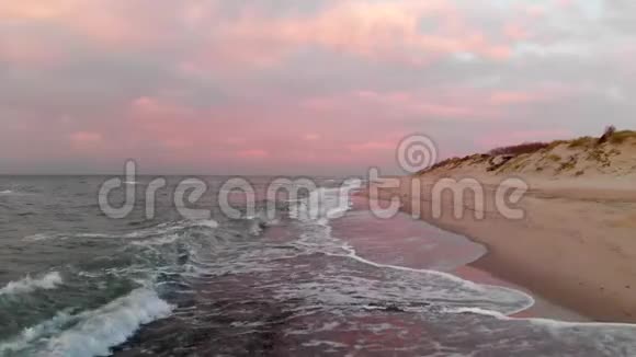 空中观看无人机镜头低飞行在一个废弃的海滩上日落带着滚滚波浪和粉红云彩的沙滩视频的预览图