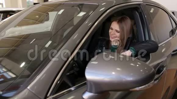 幸福的女孩坐在现代陈列室的一辆新车的车轮后面视频的预览图