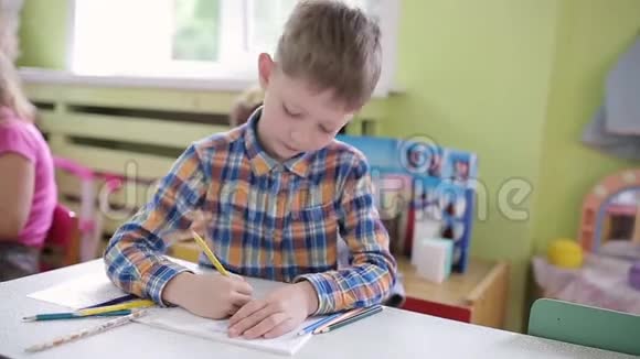 6岁的男孩在学校课桌上的一堂课上用笔记本做作业学前教育视频的预览图