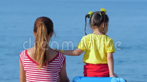 小可爱的女孩和她穿着五颜六色衣服的妈妈坐在海滩上视频的预览图