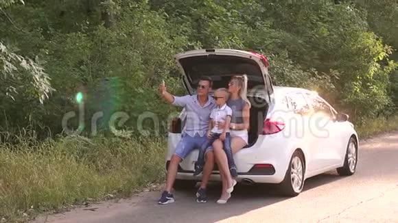 一个幸福的家庭和他们的儿子坐在汽车的后备箱里自拍旅行视频的预览图
