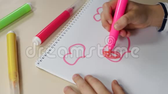 小手的特写一个孩子用一支粉红色的铅笔在桌子上的白纸上画心脏视频的预览图