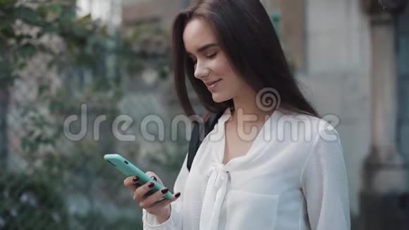 用她的现代智能手机近距离拍摄了一个漂亮的学生女孩肩膀上有一个包年轻女子在滚动视频的预览图