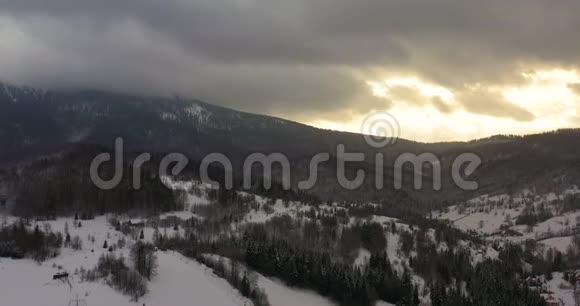 冬季日落时用雪覆盖的高山和森林的鸟瞰图视频的预览图