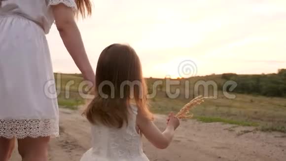 一个穿着白色连衣裙的小女儿正和她妈妈手在路上散步妇女和儿童的晚间散步视频的预览图