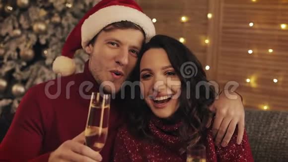 温馨舒适的家居氛围中幸福的微笑情侣捧着香槟欢乐的酒杯坐在圣诞树附近视频的预览图