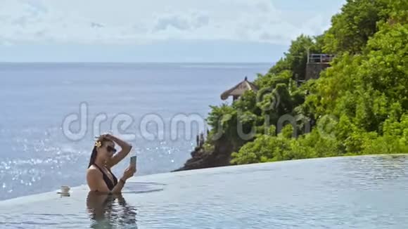 美国女商人在亚洲度假胜地的游泳池里使用智能手机进行视频通话视频的预览图
