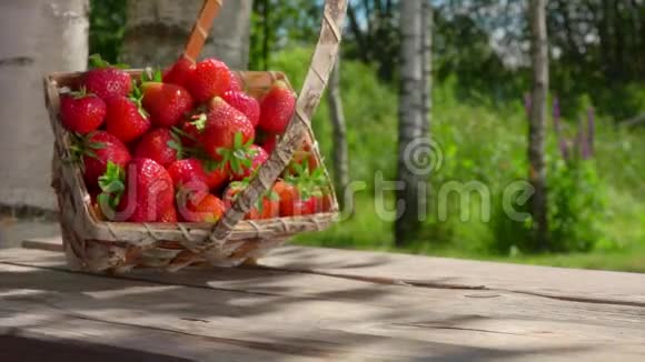 装满成熟甜草莓的篮子正落在户外的木桌上视频的预览图
