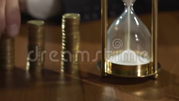 富人把硬币放在堆上看沙漏测量时间金融视频的预览图