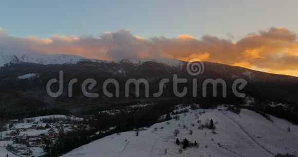 冬季日落时积雪覆盖的高山和森林的鸟瞰图视频的预览图