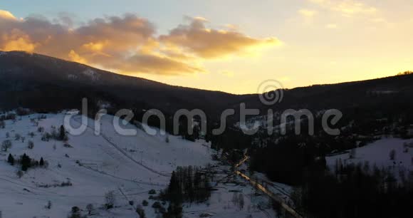 冬季日落时积雪覆盖的高山和森林的鸟瞰图视频的预览图