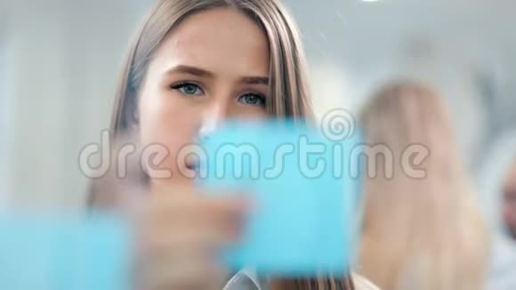 自信的年轻商务女性在玻璃板上贴着彩色黏糊糊的纸条看着头脑风暴视频的预览图