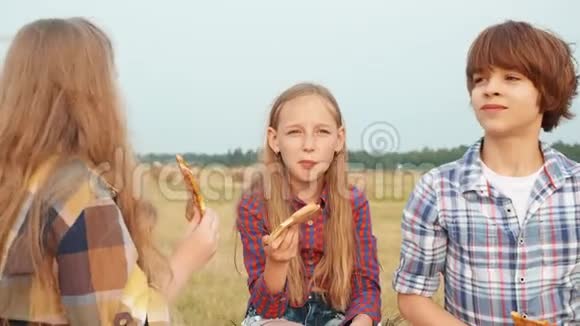 在乡间野地野餐时吃披萨的青少年朋友快乐的女孩和男孩在乡村野餐时吃披萨视频的预览图