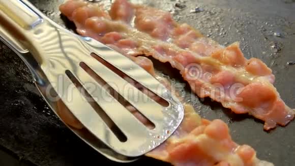 美味的油炸培根用金属舌头在石烤架上翻转视频的预览图